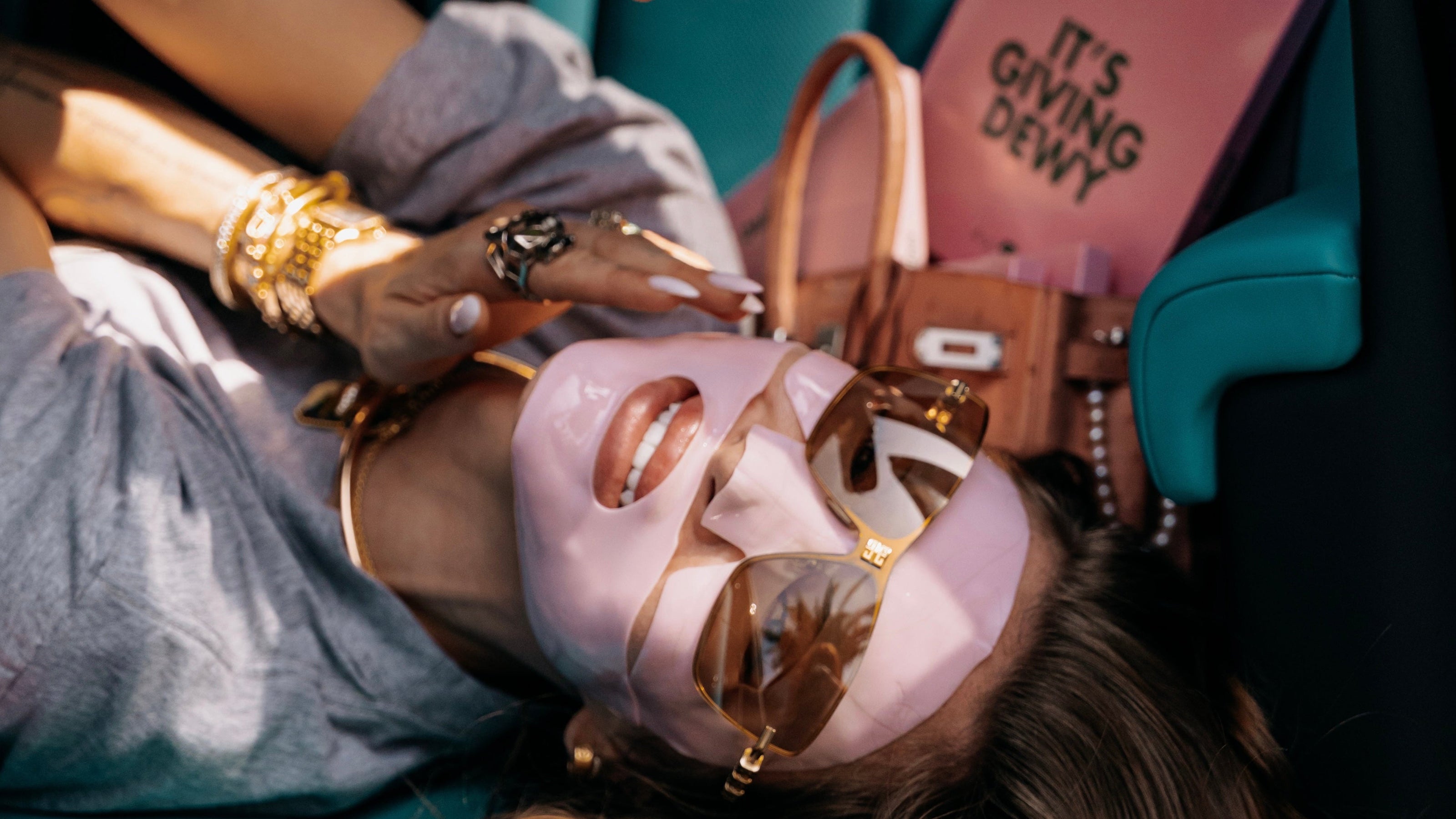 Person lying in a car with tattoos and accessories, holding a camera.